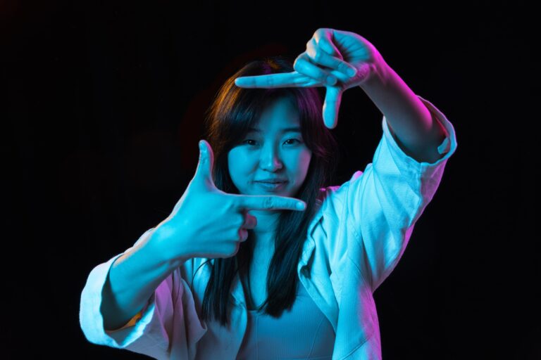 Asian young woman's portrait on dark studio background in neon. Concept of human emotions, facial expression, youth, sales, ad.